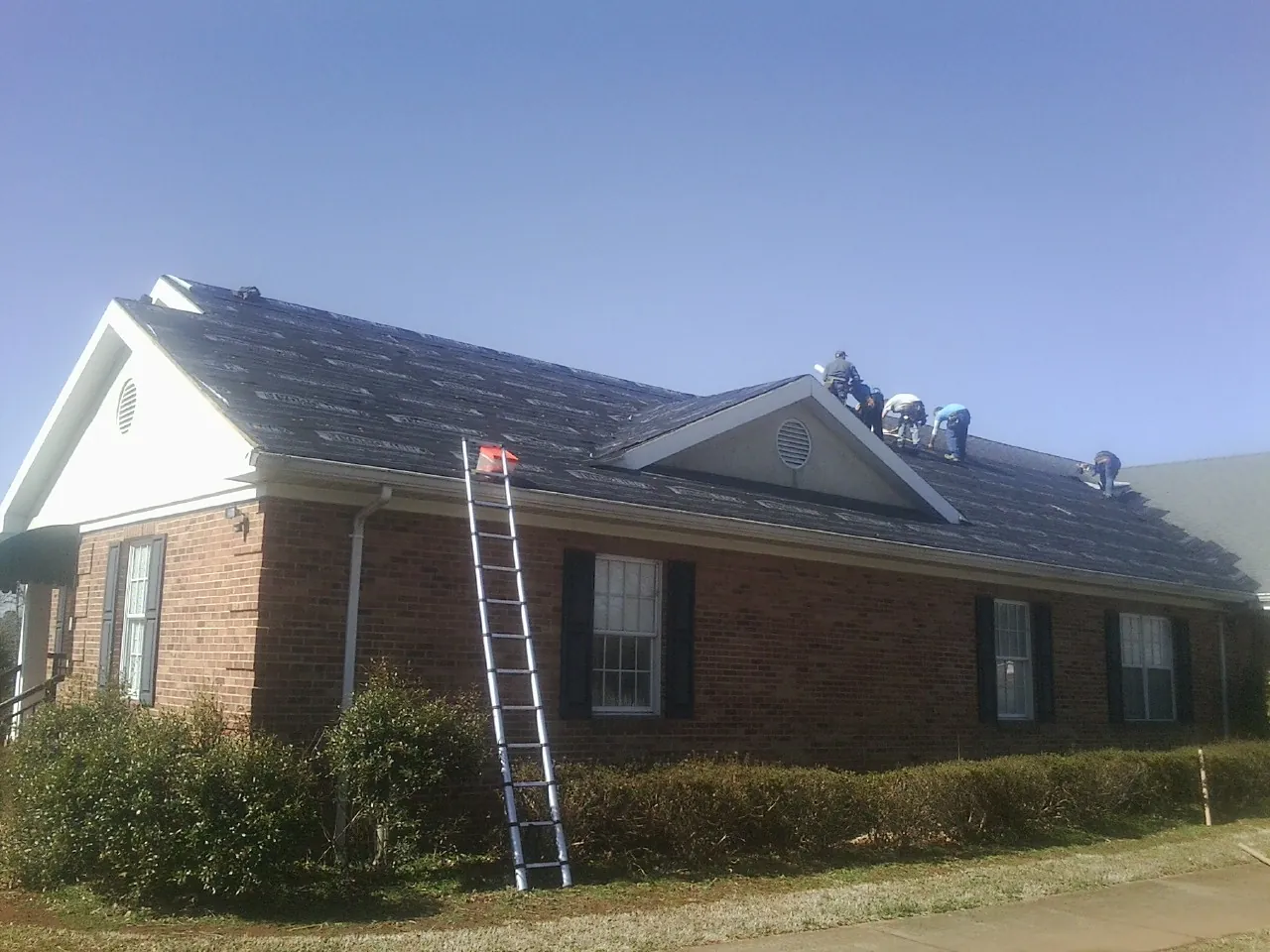 Crew tearing shingles off a brick ranch roof with a ladder set — Metal Roof Repair work by our crew in Pine Grove