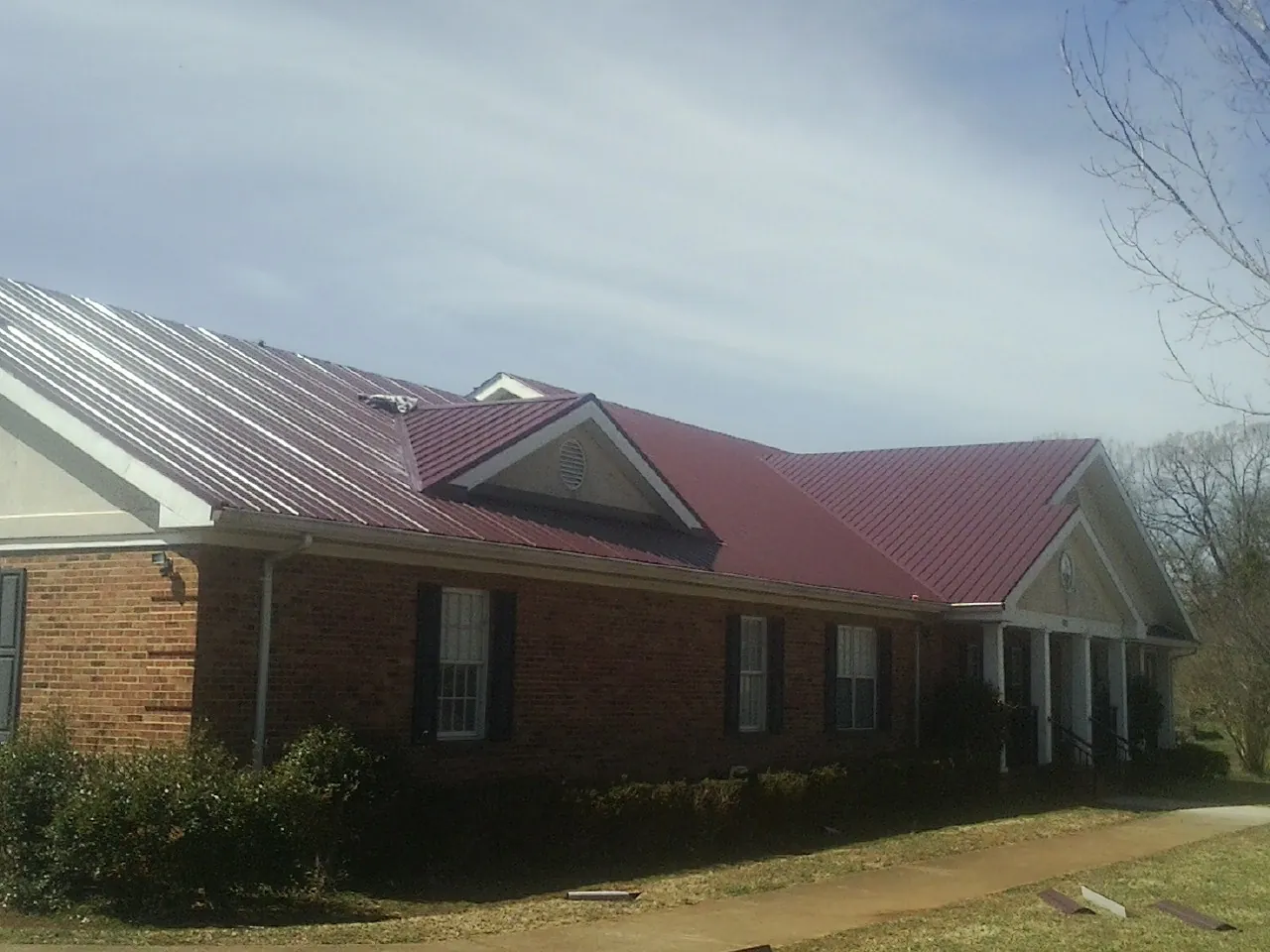 Red metal roof with gabled entries on a long brick building, from a Hail Damage Roof Repair job in Pine Grove