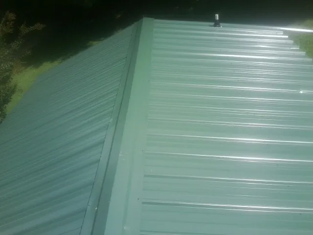 New green metal panels meeting at the ridge of a roof — Flat Roof Repair work by our crew in Pine Grove