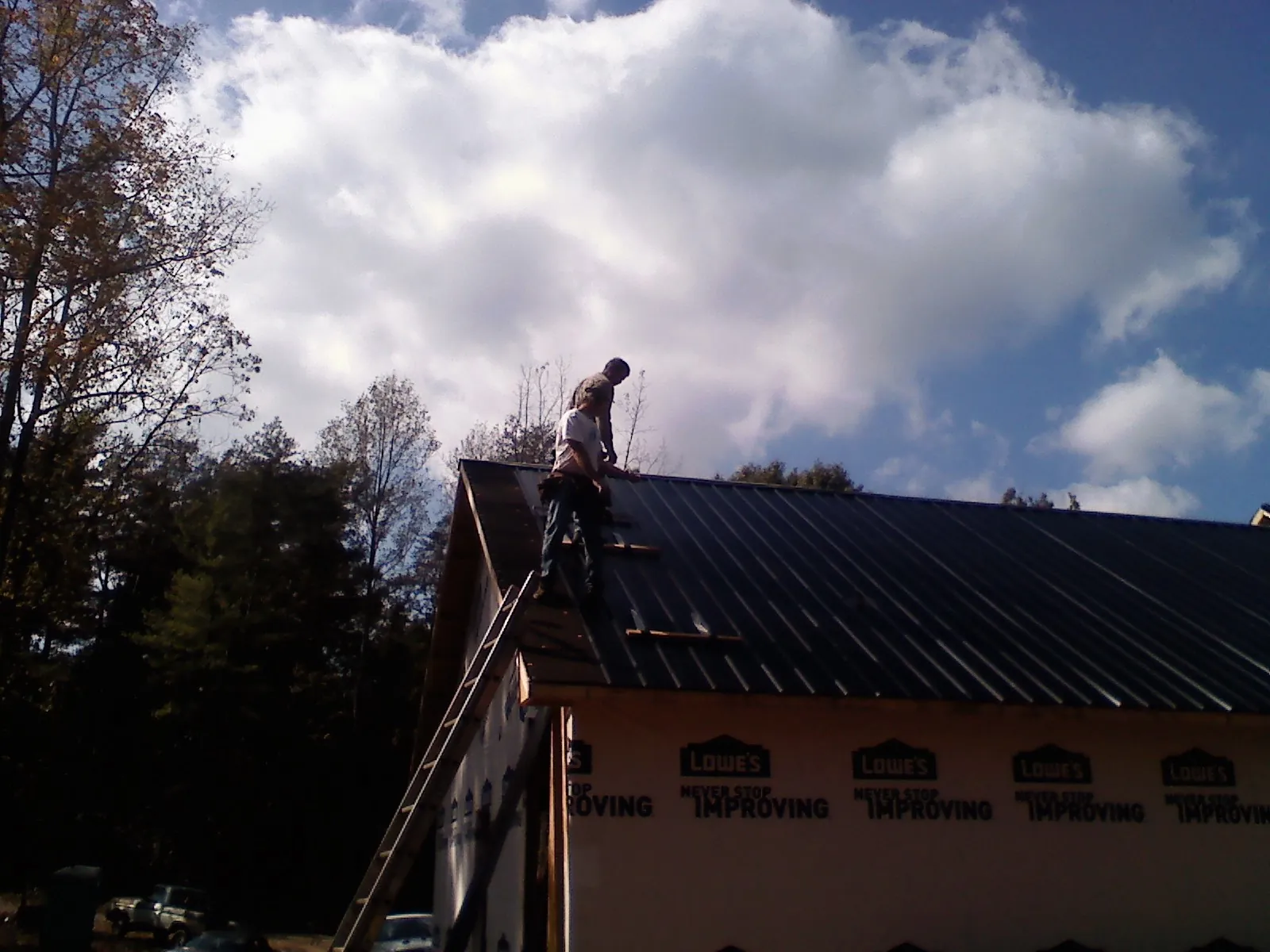 Roofer fastening dark metal panels high against a cloudy sky, from a Roof Inspection job in Pine Grove